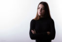 Un jeune fille sur fond blanc, les bras croisés, regarde fixement de trois quart.