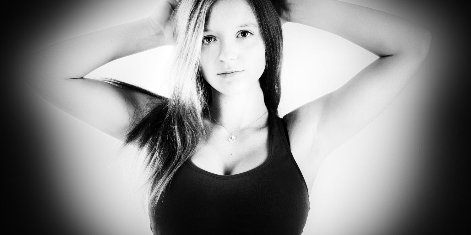 Portrait noir et blanc du visage d'une jeune fille avec un bustier de sport, les mains posées sur les cheveux