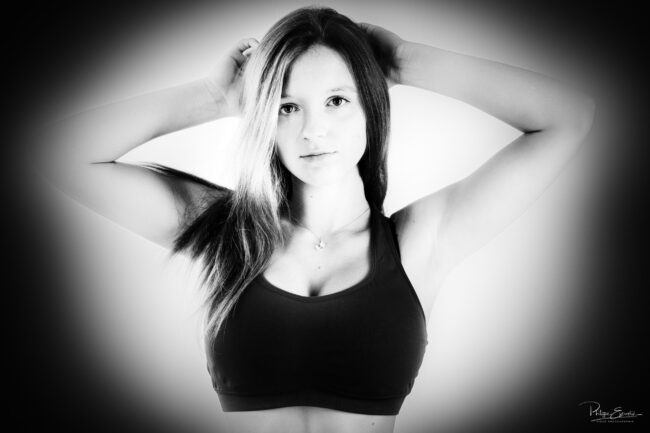 Portrait noir et blanc du visage d'une jeune fille avec un bustier de sport, les mains posées sur les cheveux