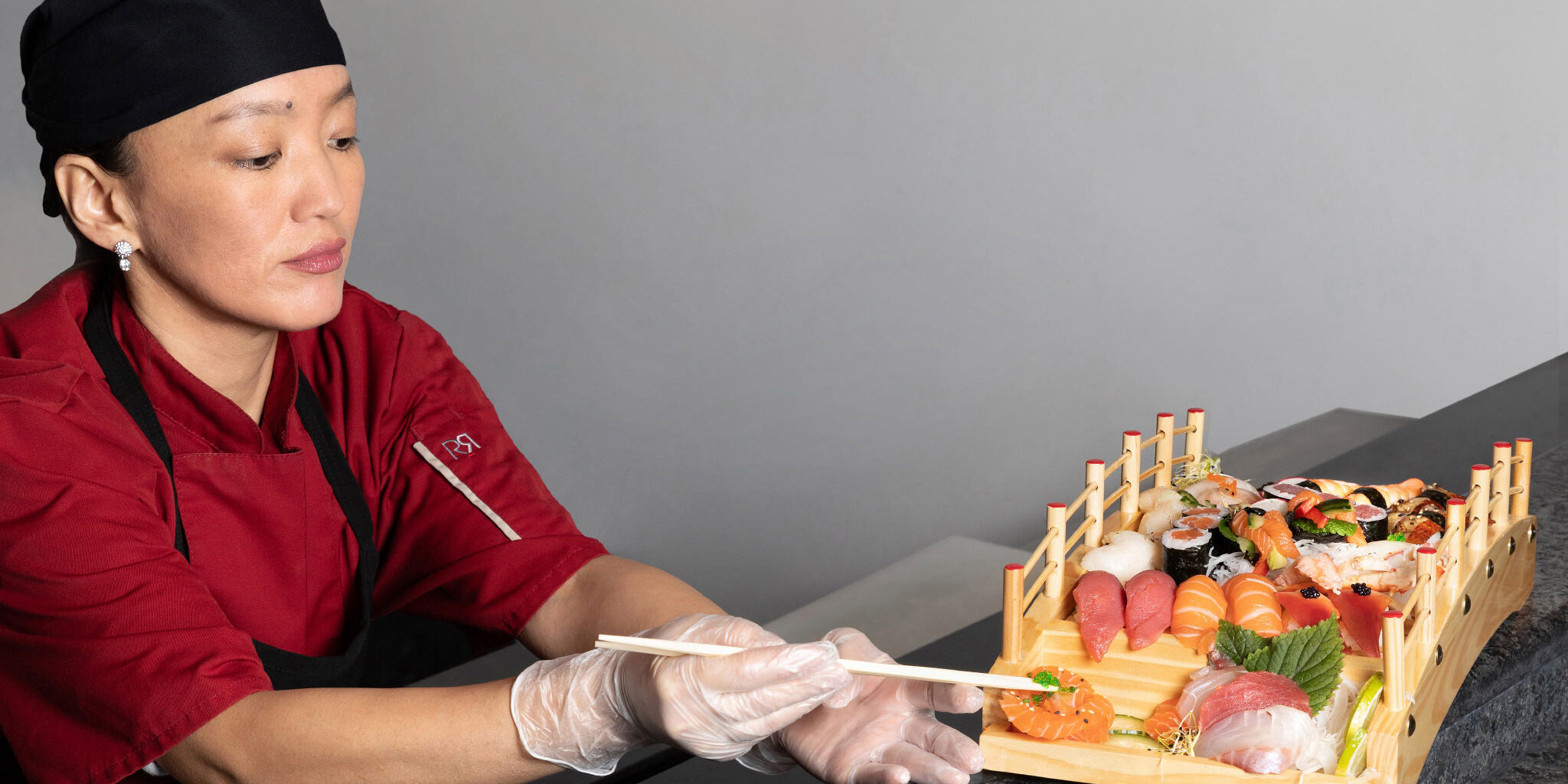 une chef cuisinière utilise des baguettes pour poser des oeufs de lompe sur un plat composé de sushis