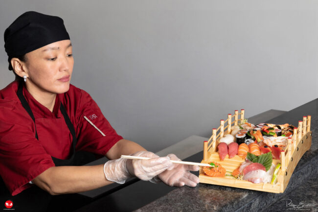 une chef cuisinière utilise des baguettes pour poser des oeufs de lompe sur un plat composé de sushis