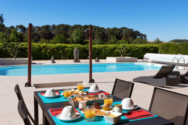 Table en terrasse avec petit dejeuner servi et piscine en arrière plan