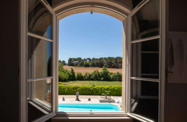 fenêtre ouverte avec vue sur une piscine et des montagnes à l'horizon