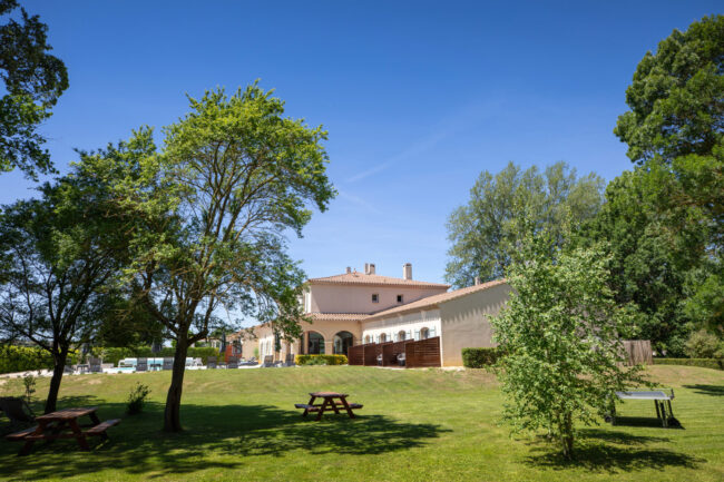 Parc arboré avec un banc au milieu et une maison derrière