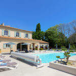 piscine de jour avec végétation en premier plan et une maison derrière