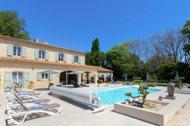 piscine de jour avec végétation en premier plan et une maison derrière