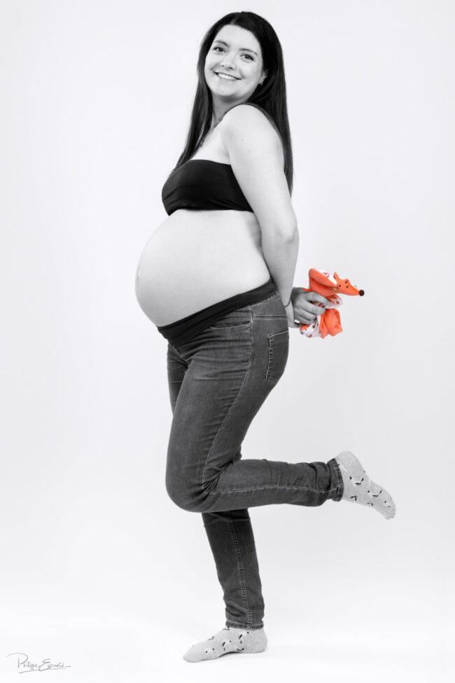 Une femme enceinte en noir et blanc tient dans son dos un doudou en couleur
