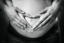 Deux mains en forme de coeur tenues sur le ventre d'une femme enceinte