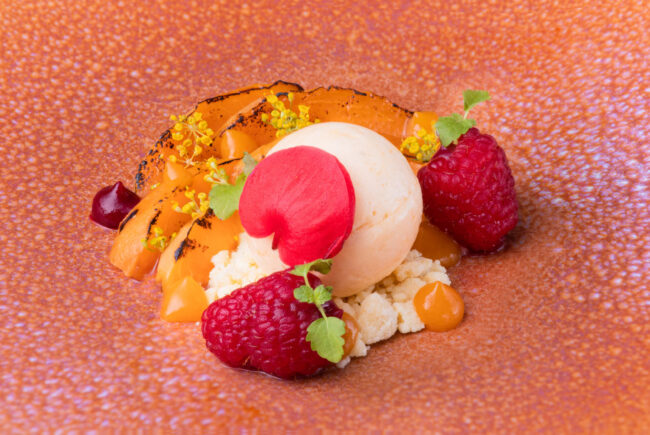 Dans les cuisines du Puits du Trésor, Lastours 12 Dessert composé de deux framboises entières, d'abricots caramélisés, de crumble au chocolat blanc et d'une boule de glace de vanille