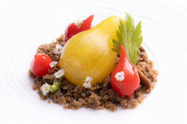 Trois mini tomates rouges et une tomate poire disposées dans une assiette sur un lit d'aubergine avec des petits fleurs blanches autour