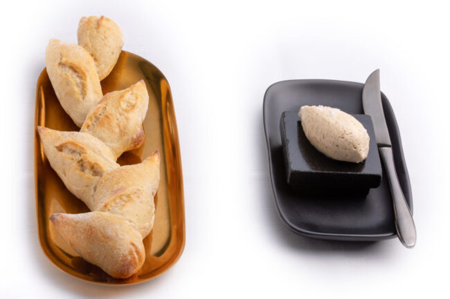 Dans les cuisines du Puits du Trésor, Lastours 13 pain en épi dans une corbeille avec à côté du beurre salé et un couteau sur un beurrier noir