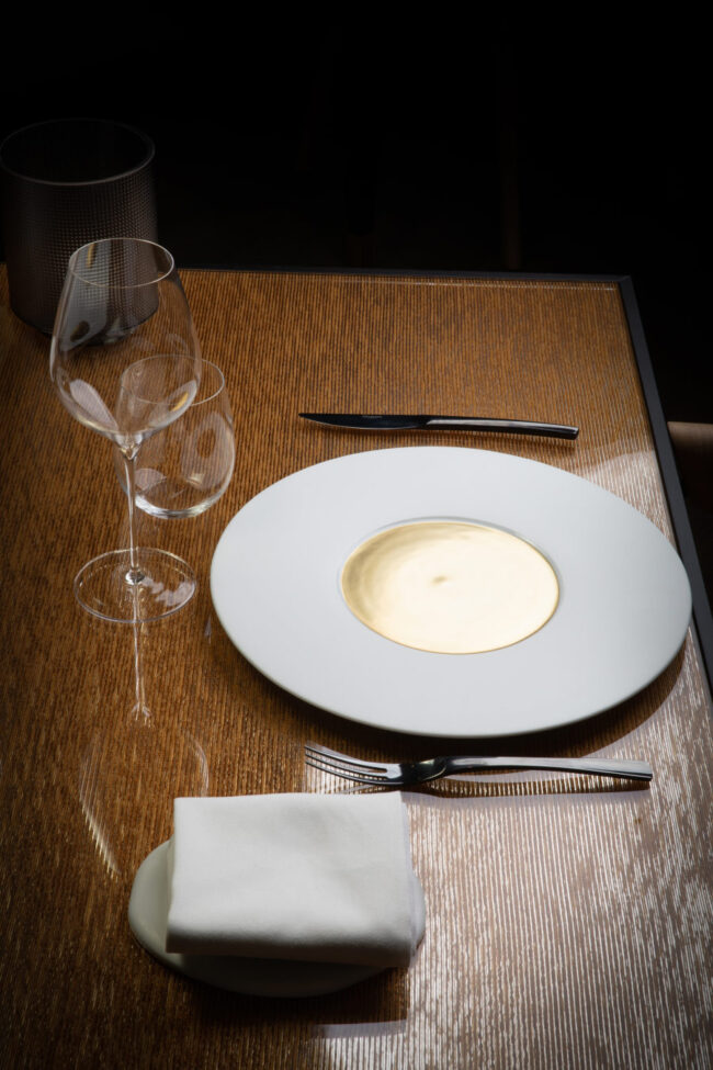 Restaurant Le Puits du Trésor, Lastours 5 Assiette blanche avec au centre un rond dorée en atmosphère contre jour