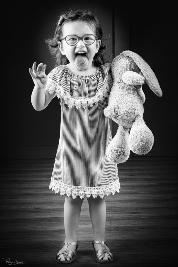 Une petite fille tient un lapin en peluche dans les mains et tire la langue