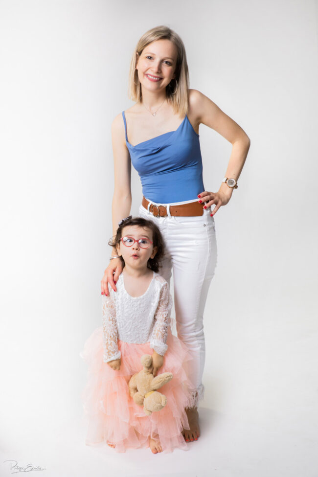 En famille, formule box cadeau ! 14 Une maman est debout avec sa fille. La maman a la main sur l'épaule de la fille et la fille tient un ours en peluche dans sa main.