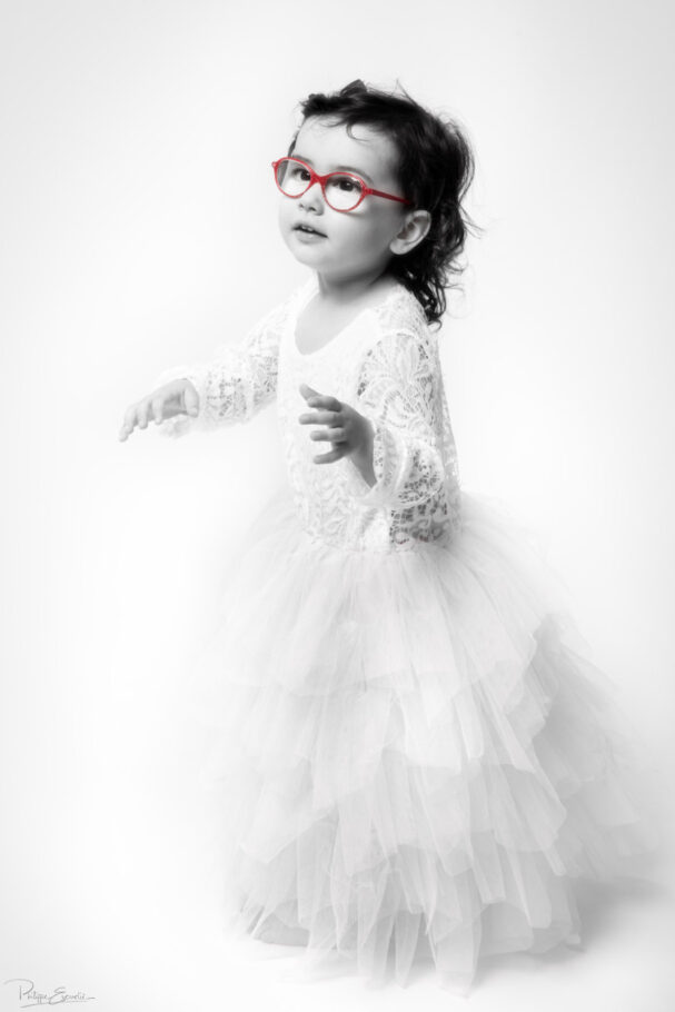 Une petite fille est debout habillée en blanc avec des lunettes rouges