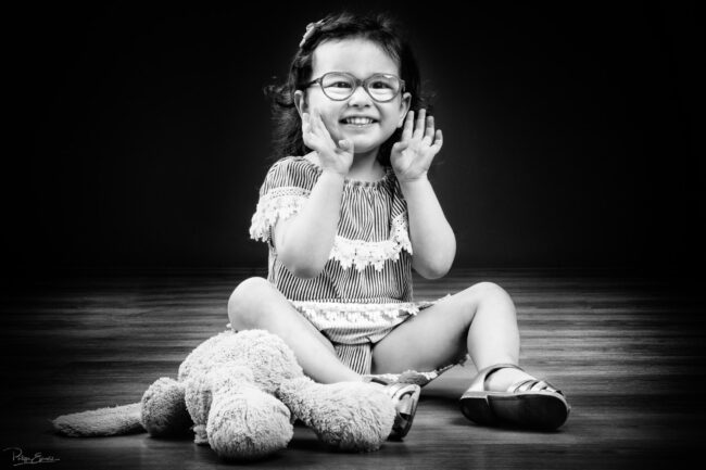 En famille, formule box cadeau ! 19 Une fillette assise sur un parquet en bois a les mains devant la bouche