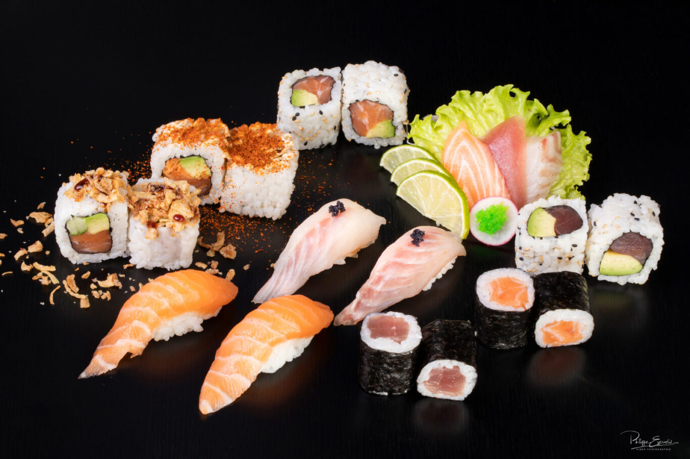 Un assortiment de sushis posés sur une table noire avec des oignons frits et de la poudre de paprika en décoration.