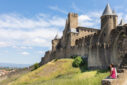 Une fille est assise devant les remparts d’une cité médiévale