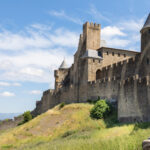 Une fille est assise devant les remparts d’une cité médiévale