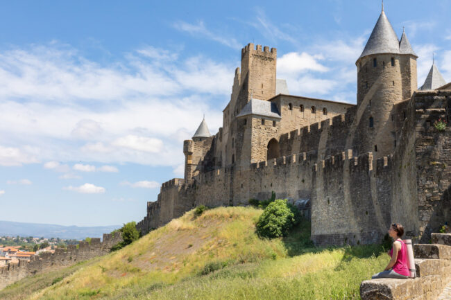 Une fille est assise devant les remparts d’une cité médiévale