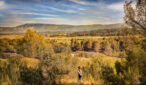 Une fille de dos, debout dans la nature, un tapis de yoga sur les épaules, regarde un paysage panoramique montagneux