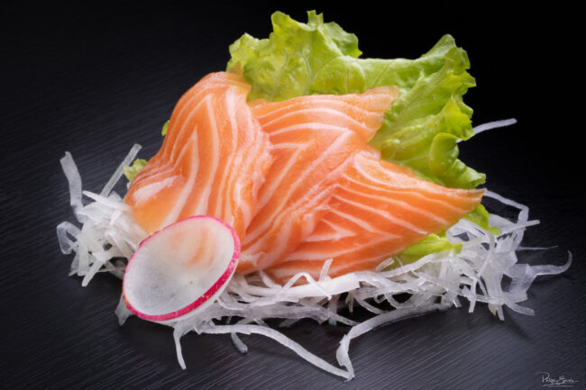 Shooting culinaire pour le restaurant An Sushi 4 Un sahsimi posé sur fond noir, réalisé avec trois tranches de saumon, une feuille de salade et un rondelle d'oignon