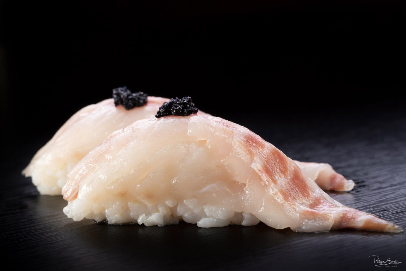 Deux sushis réalisés avec du bar et du riz, posés sur une table noire