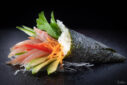 Un temaki en forme de cone, posé sur une table noire, avec à l'intérieur de fines tranches de thon, tomate, carotte et feuille de menthe.