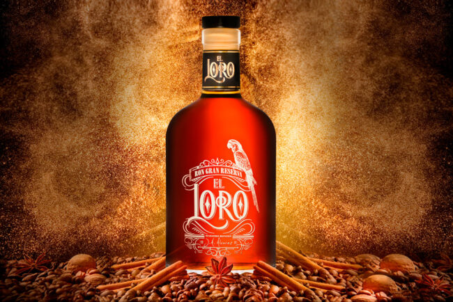 Une Bouteille de rhum est posée sur un monticule composé de noix, de bâtons de cannelle et grain de café.