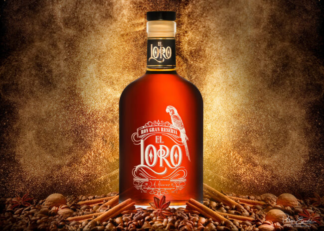 Shooting de bouteilles avec mise en scène pour la Société RF Distribution 2 Une Bouteille de rhum est posée sur un monticule composé de noix, de bâtons de cannelle et grains de café, avec en arrière-plan une explosion de poudre d’or