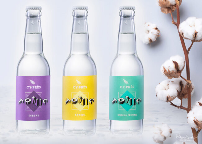 Shooting de bouteilles avec mise en scène pour la Société RF Distribution 3 Trois bouteilles de tonic translucides sont posées sur un fond givré et humide et sur la droite une branche avec des fleur de coton.