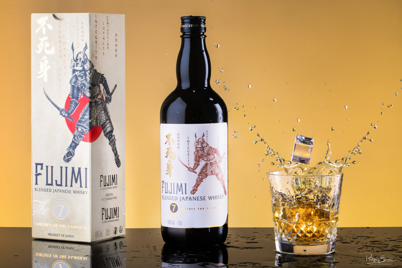 Une bouteille de whisky avec à côté une boite d’emballage à l’effigie d’un samouraï. A droite de la bouteille il y a un verre dans lequel un glaçon lancé projette des éclaboussures de whisky.