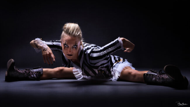 Isa Joker Shooting Studio 11 Une femme en costume rayé noir et blanc est assise sur le sol en position de grand écart