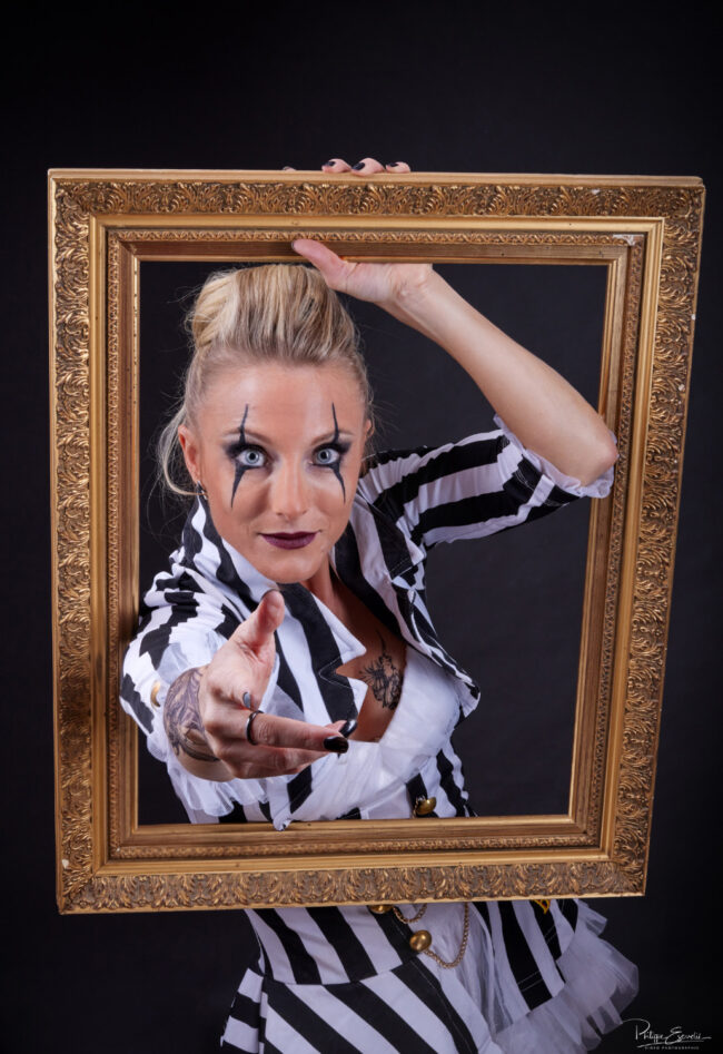Isa Joker Shooting Studio 7 Une femme blonde derrière un cadre en bois tend sa main à travers le cadre en direction du spectateur
