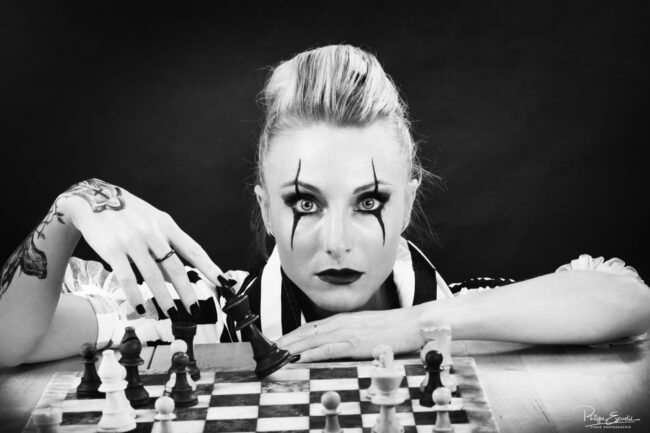 Isa Joker Shooting Studio 8 Ambiance noir et blanc, une fille est accroupie derrière un échiquier.