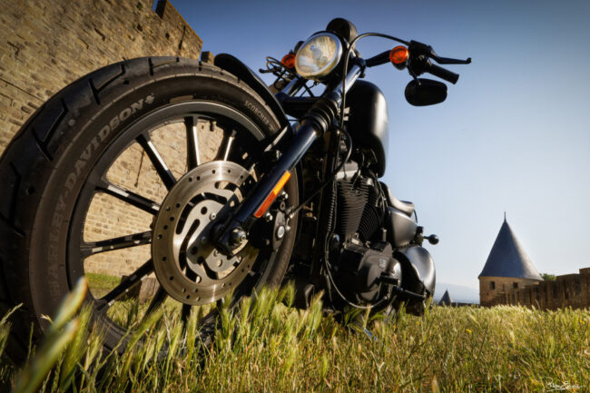 Une moto sur l’herbe vue du sol en contre plongé avec des remparts de pierre en arrière-plan