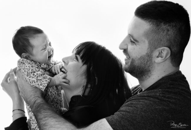 Séance photo nouveau-né et parents 8 Un bébé est tenu en l’air par ses deux parents qui le regardent en souriant