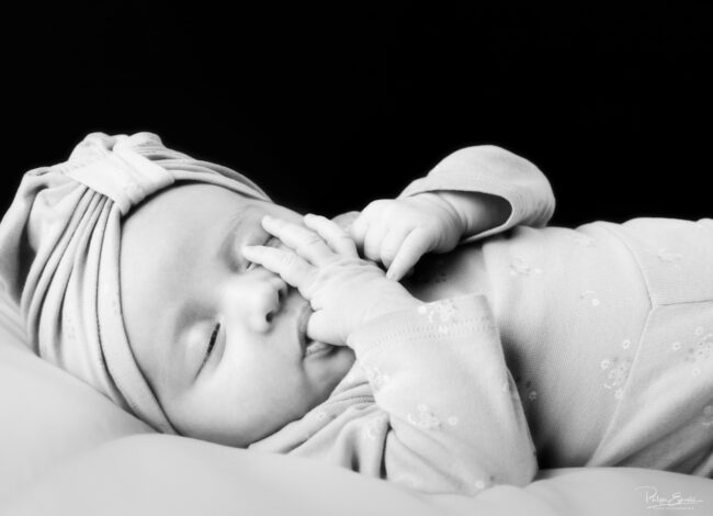 Séance photo nouveau-né et parents 4 Un bébé avec un turban sur la tête est allongé et suce son pouce