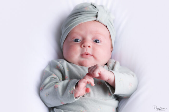 Séance photo nouveau-né et parents 6 Un bébé au regard surpris est allongé sur le dos sur une couette blanche