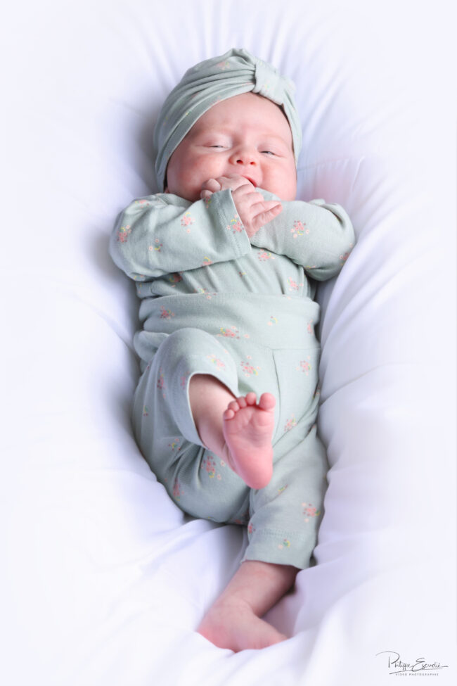 Séance photo nouveau-né et parents 7 Un bébé au regard souriant en pyjama vert est allongé sur le dos sur une couette blanche