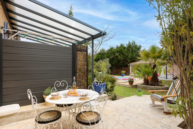 Shooting immobilier, pour maisons d’hôtes, gîtes, hôtels, propriétaires ou conciergerie. 12 Terrasse d’extérieur avec une table en fer sur laquelle un petit déjeuner est présenté et une piscine en arrière-plan.