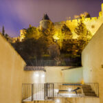 Terrasse de nuit aux murs jaunes avec un jacuzzi éclairé et la cité de Carcassonne en arrière-plan.