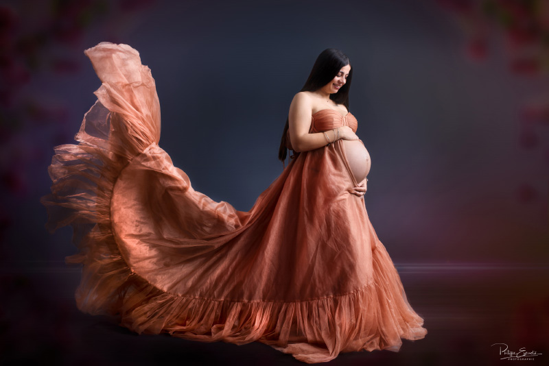 Femme enceinte avec une longue robe en mouvement les mains posées sur son ventre