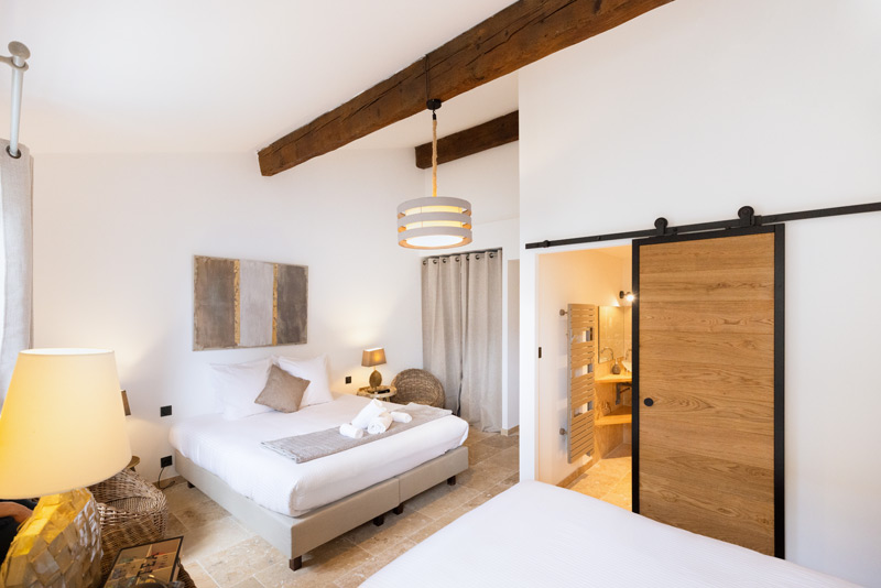 Chambre à coucher avec murs blancs , grand lit et une salle d'eau dévoilée par une porte coulissant en bois