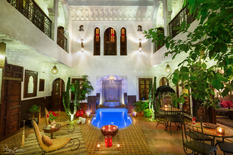 Patio d'un riad de nuit avec piscine, la cours du patio est décorée de bougies et de végétation