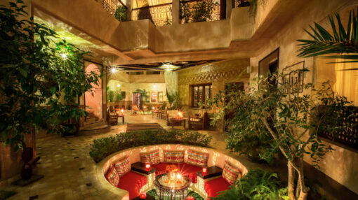 Patio d'un Riad de nuit avec un salon circulaire et des alcoves ornées de bougies et de végétation