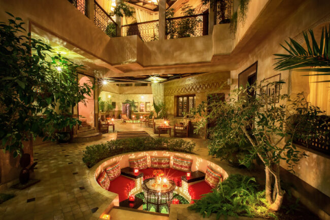 Patio d'un Riad de nuit avec un salon circulaire et des alcoves ornées de bougies et de végétation