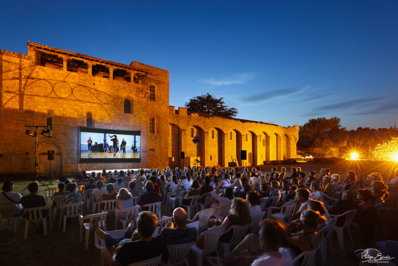 Public assis sur des chaises assistant à une projection nocturne en plein air consacrée à la dance hip hop