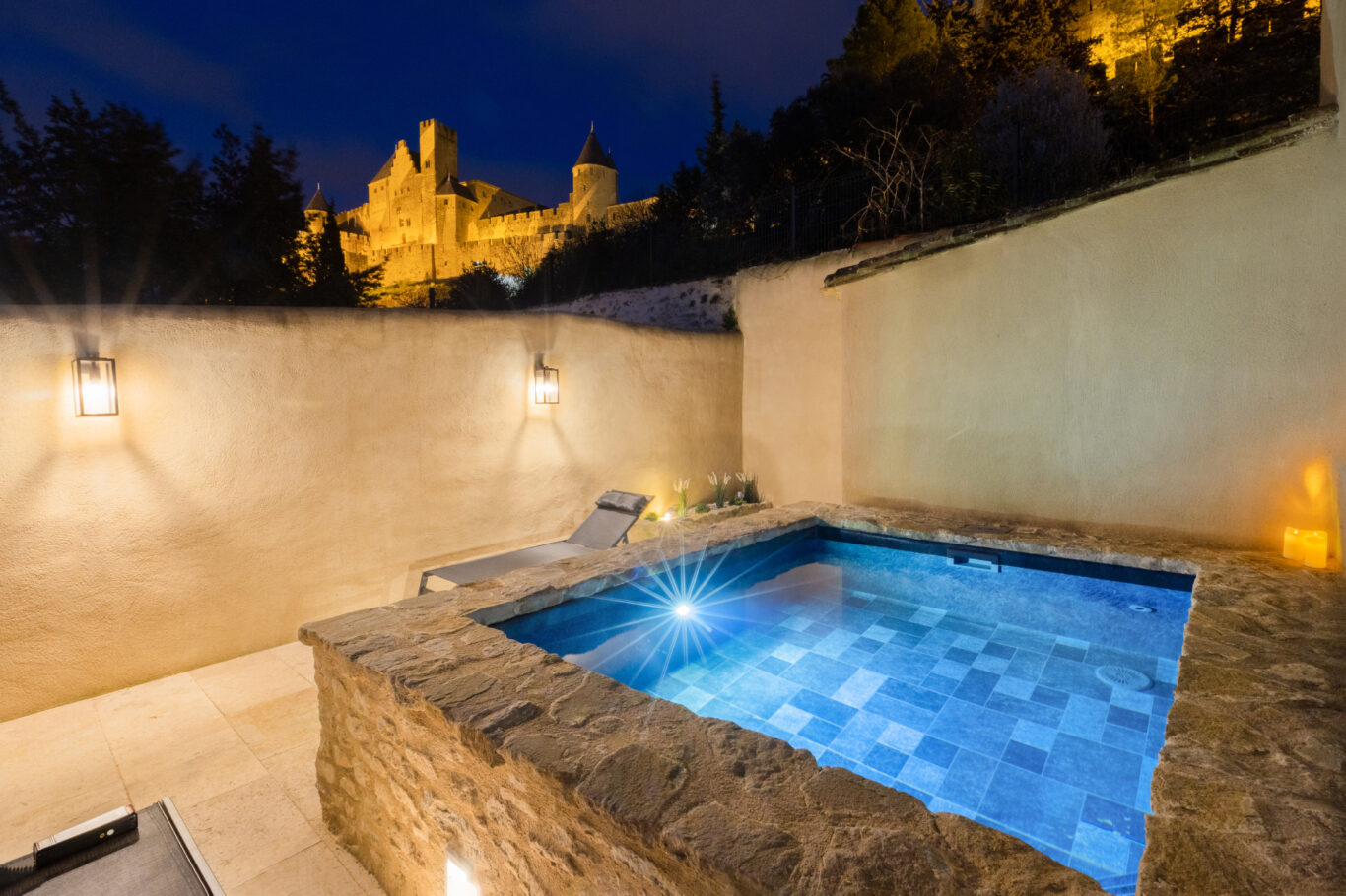 photo nocturne d'une piscine balnéo en pierre avec une eau très bleue et en arrière plan le château comtal de la cité de Carcassonne