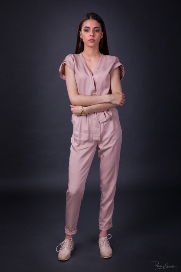 photo de studio sur fond gris d'une femme en combinaison rose les bras croisés